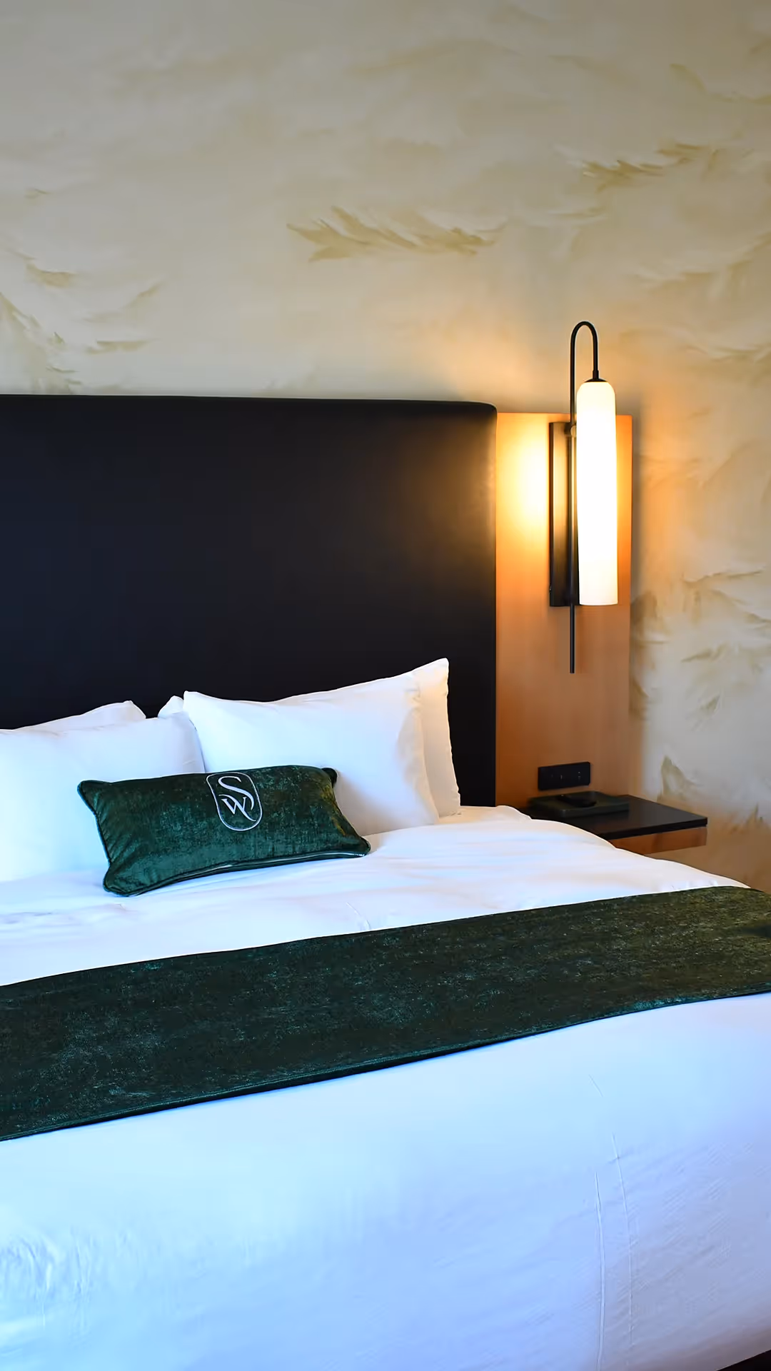 Luxury bedding at The Swiftwater hotel with emerald green runner, "SW" branded pillow, and designer bedside lamps.