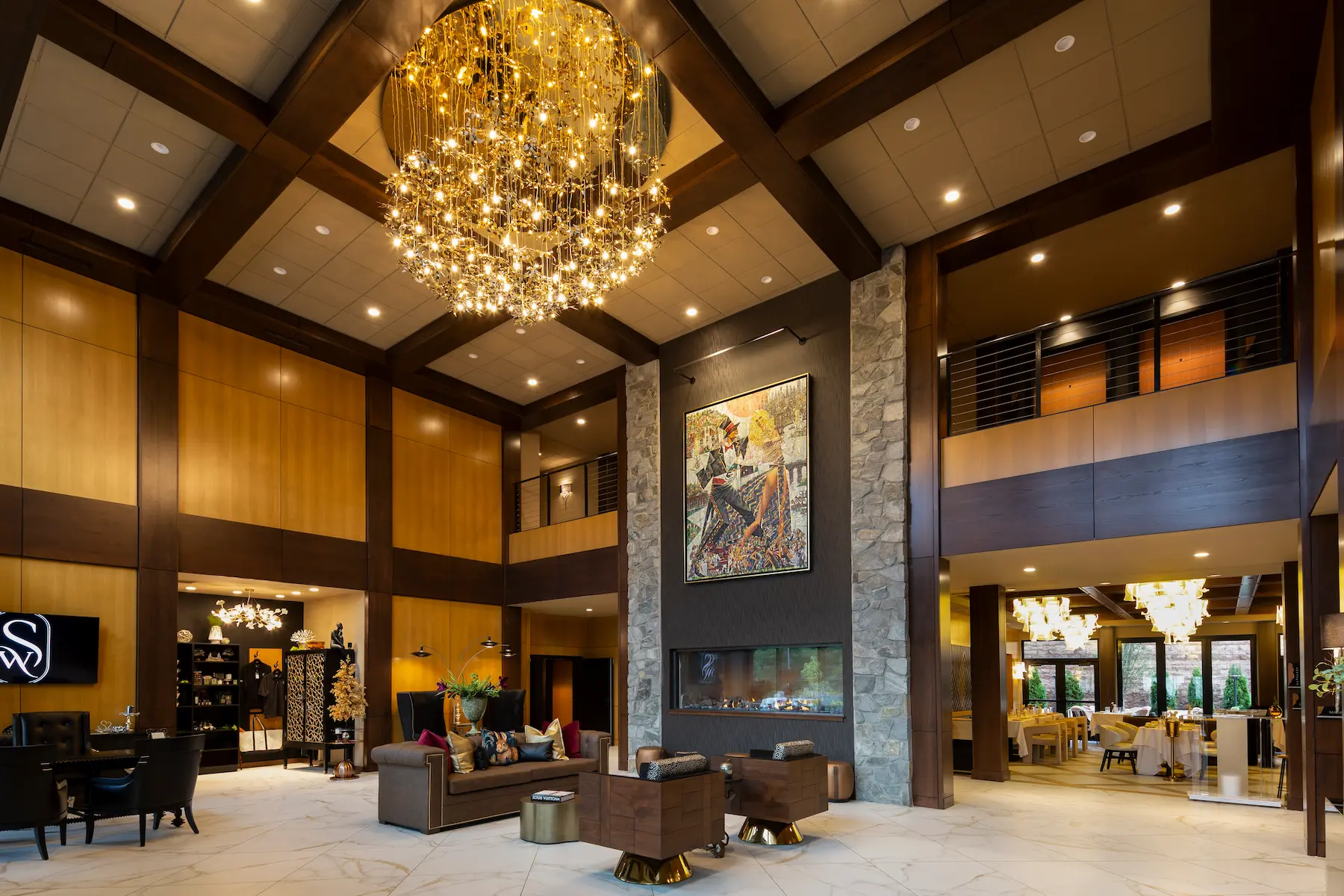 A large stone outdoor fire pit at The Swiftwater Hotel featuring tipi-style sculpted logs and warm flames, surrounded by modern lounge chairs under soft evening lighting.