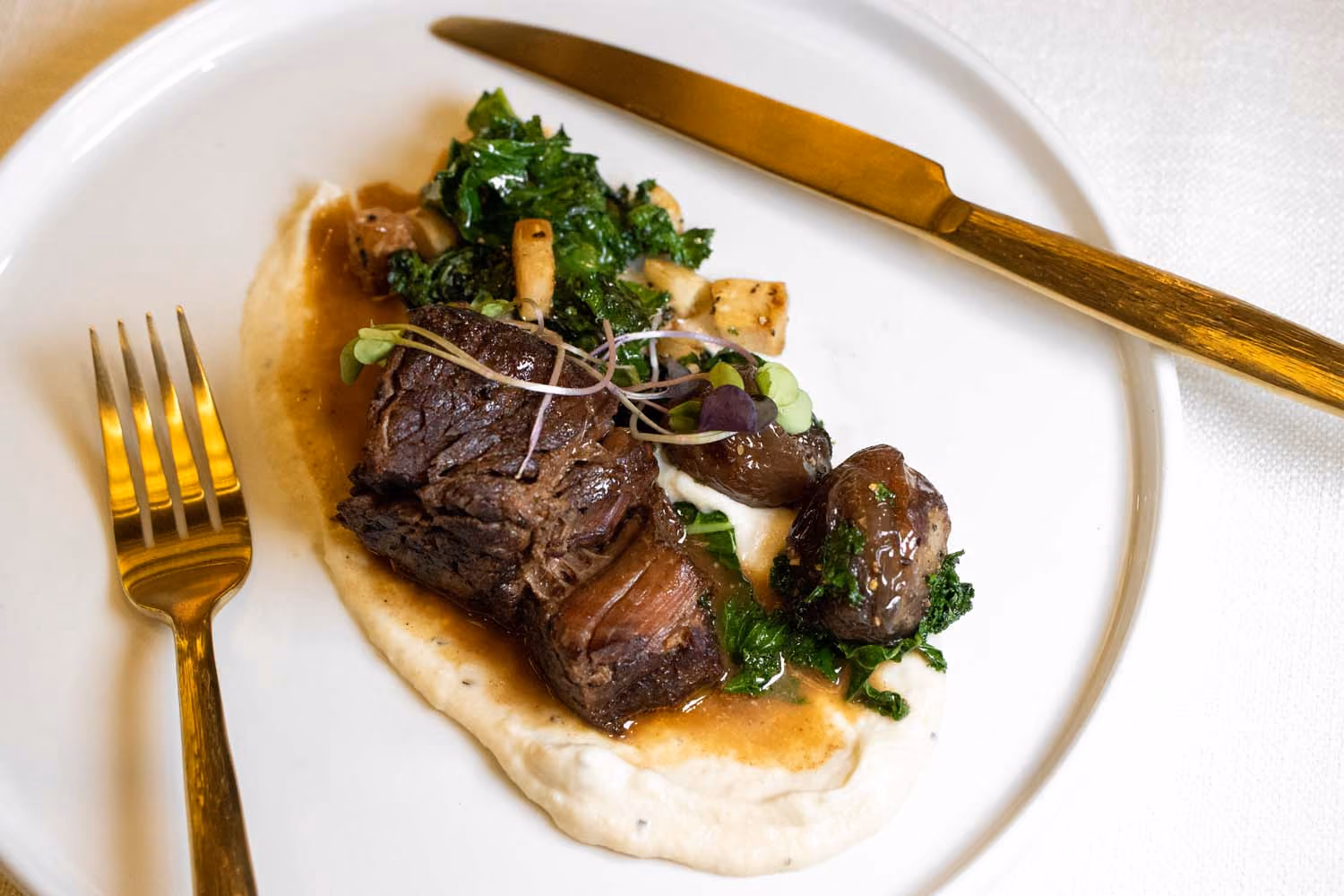 Close-up of a guest slicing into a juicy steak with gold cutlery at The Swiftwater Hotel.