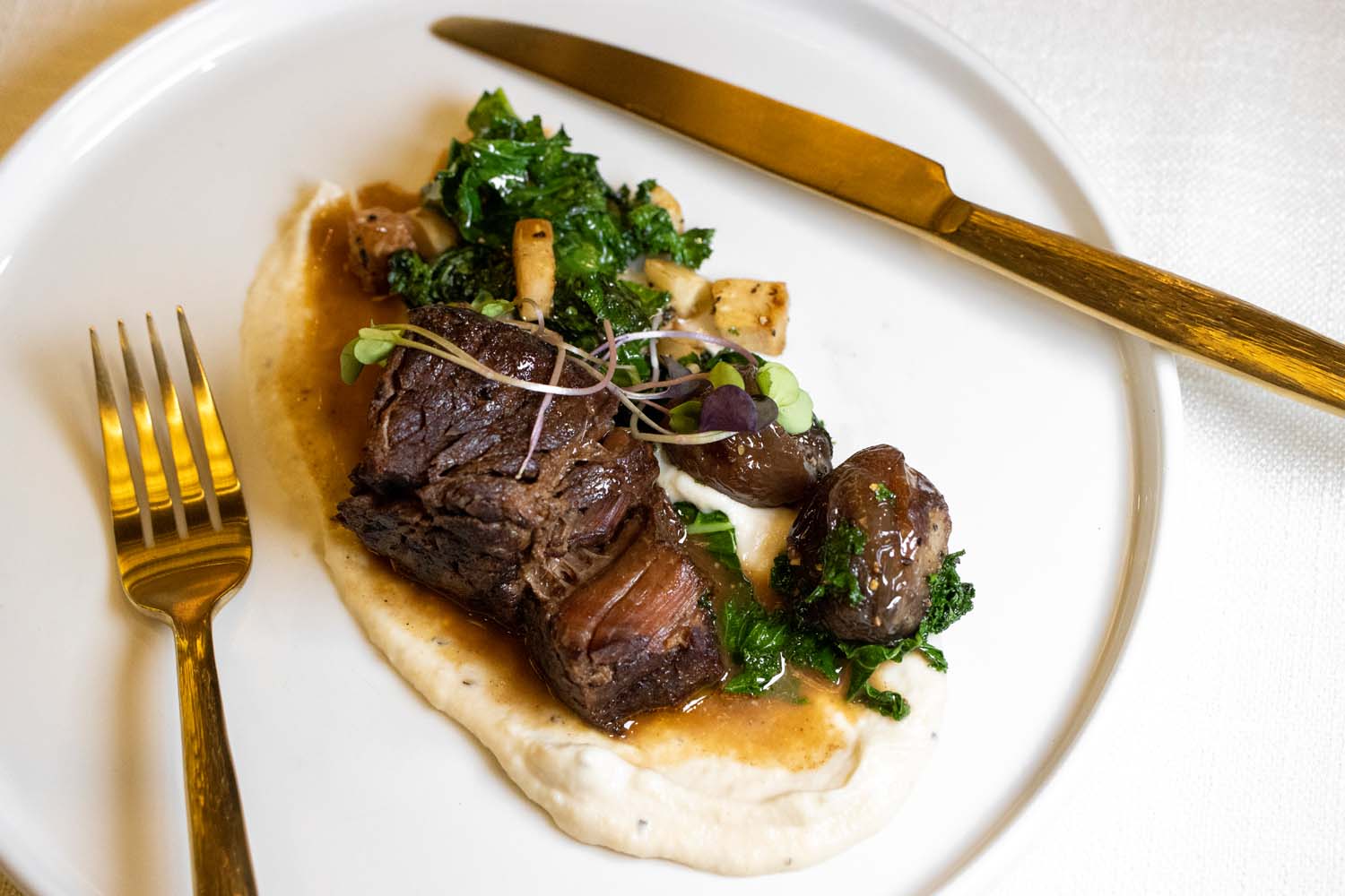 Close-up of a guest slicing into a juicy steak with gold cutlery at The Swiftwater Hotel.