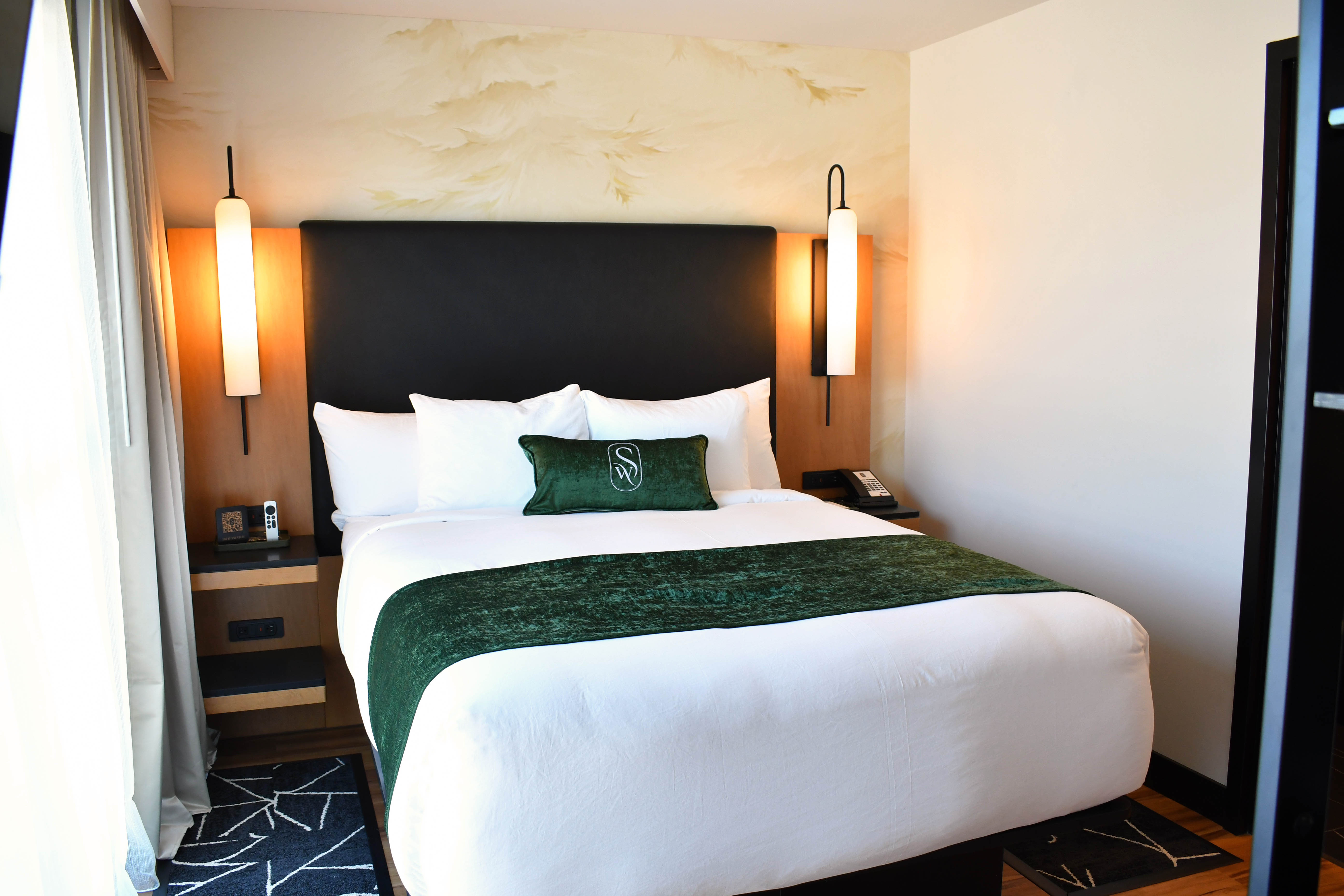 Luxurious living area at The Swiftwater hôtel featuring emerald green velvet armchairs, a modern crystal chandelier, and a wall-mounted screen displaying a pine forest, showcasing the hotel's elegant and cozy interior design.