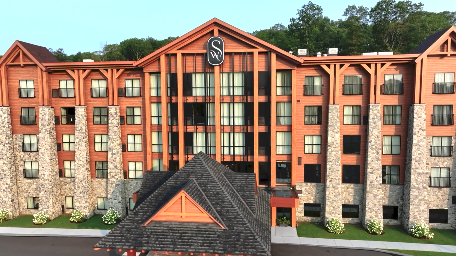 Aerial view of Swiftwater Hotel surrounded by dense forest, with a large parking lot and a road stretching into the distance under a cloudy sky. 