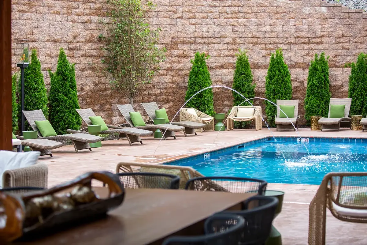 Outdoor stone fire pit surrounded by green woven lounge chairs on The Swiftwater's patio, a relaxing amenity for guests exploring Swiftwater, PA.