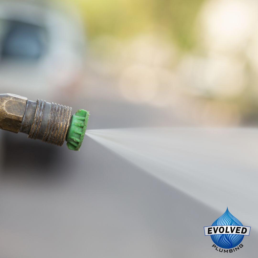 Close-up of a green spray nozzle releasing a fine mist of water, with a blurred background and Evolved Plumbing logo in the bottom right.