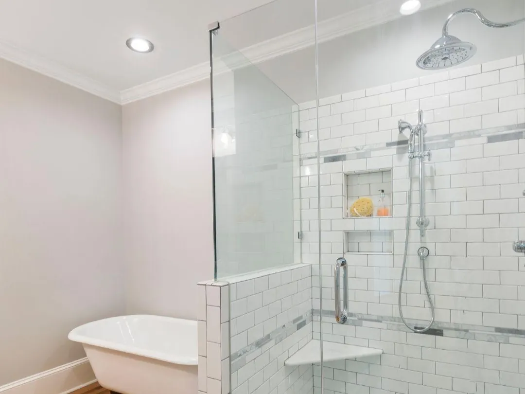 Modern bathroom with white freestanding bathtub and glass-enclosed shower featuring subway tile and chrome fixtures.