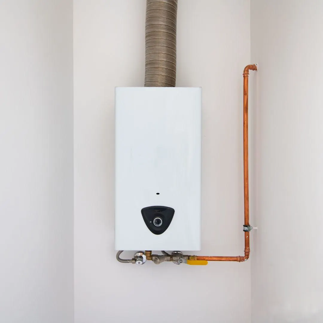 White tankless water heater mounted on a wall with connected copper piping and a vent pipe above.