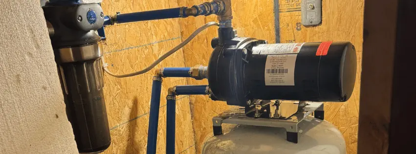 Outdoor plumbing setup showing a brass Wilkins valve connected to blue and red pipes on a dirt ground.