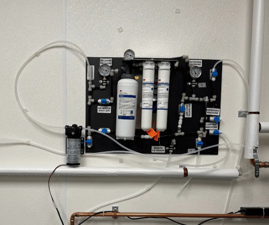 Basement corner with white PVC plumbing pipes running along a discolored concrete block wall and stained floor.