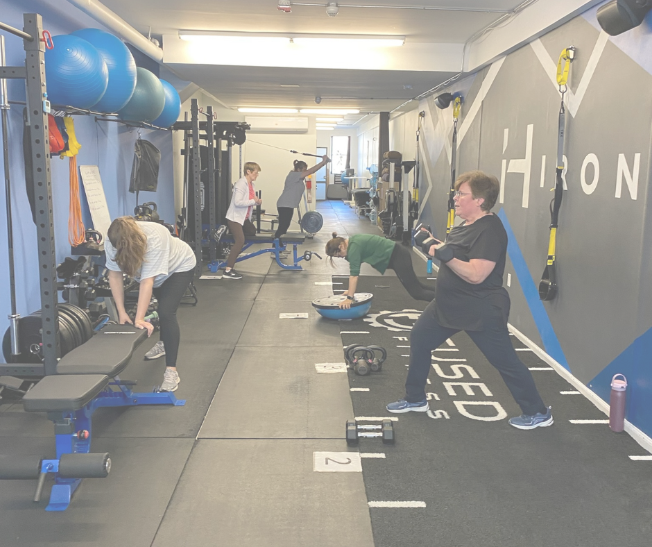 Four women exercising in a gym using various equipment including weights, a balance trainer, and resistance bands.