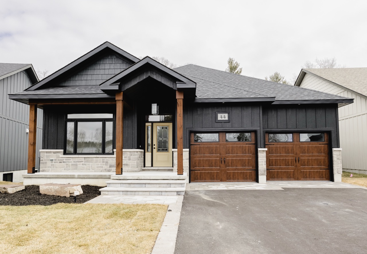 Modern house with black exterior, wooden pillars, a beige front door, and double wooden garage doors.