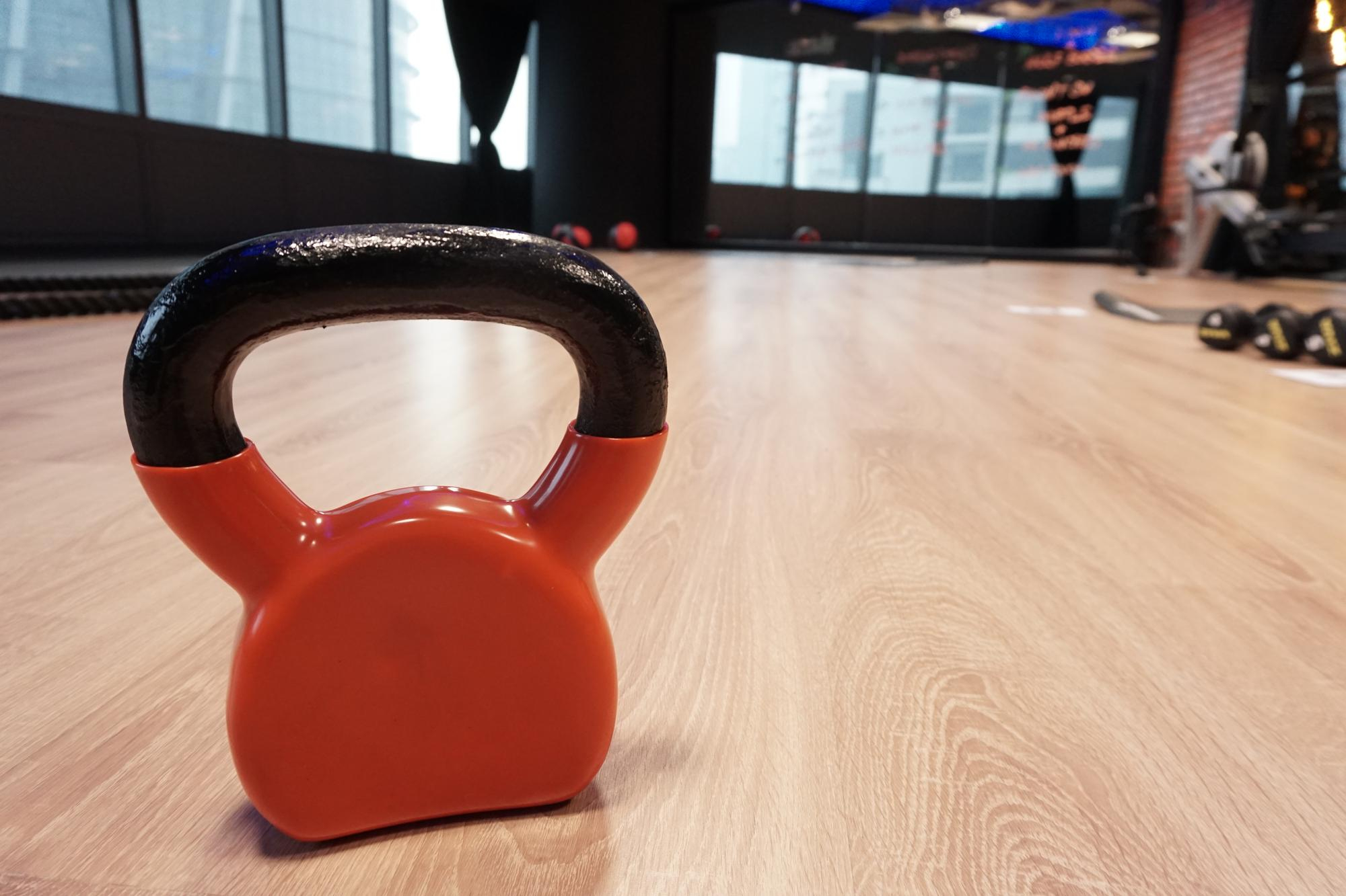 Orange kettlebell with black handle on a wooden floor in a gym.