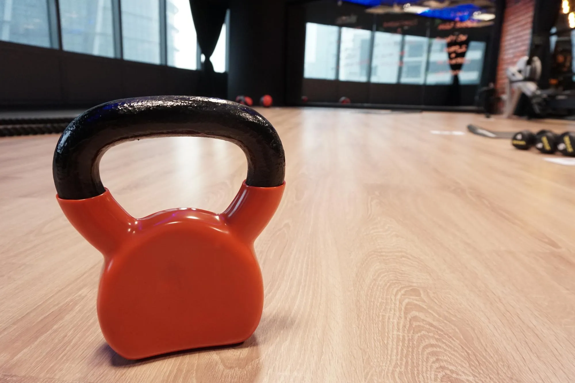 Orange kettlebell with black handle on a wooden floor in a gym.