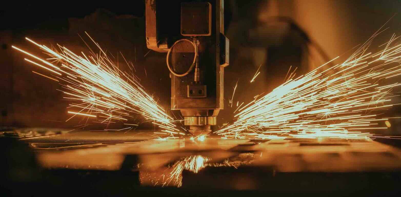 Close-up of industrial machine cutting metal with bright sparks flying outward.