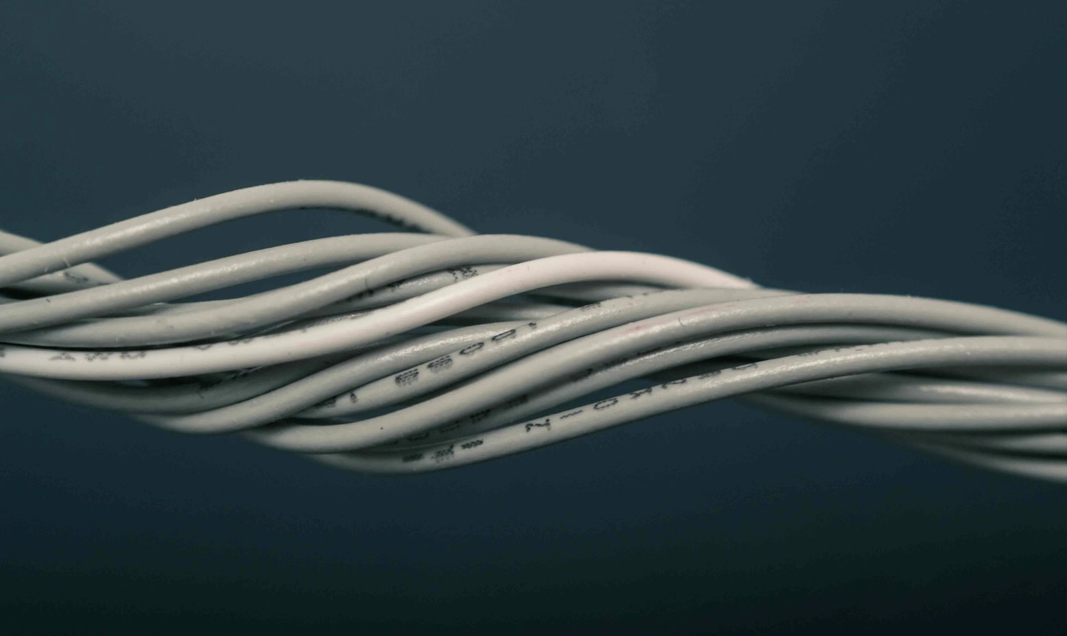 Close-up of multiple twisted white electrical cables against a dark background.