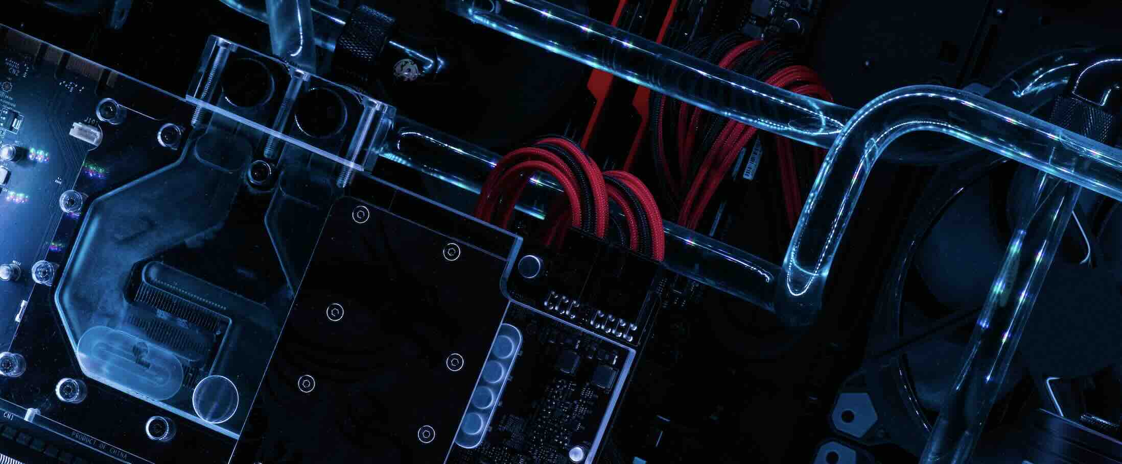 Close-up of a computer motherboard with red cables and transparent cooling tubes illuminated by blue light.