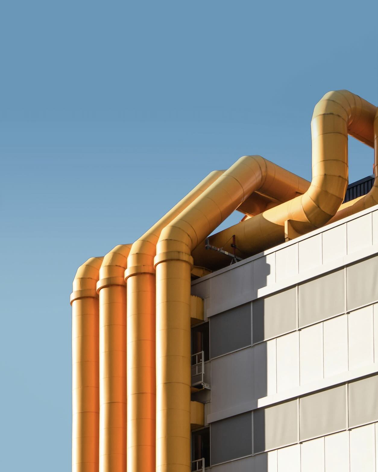 Close-up of a building with large yellow industrial pipes against a clear blue sky.