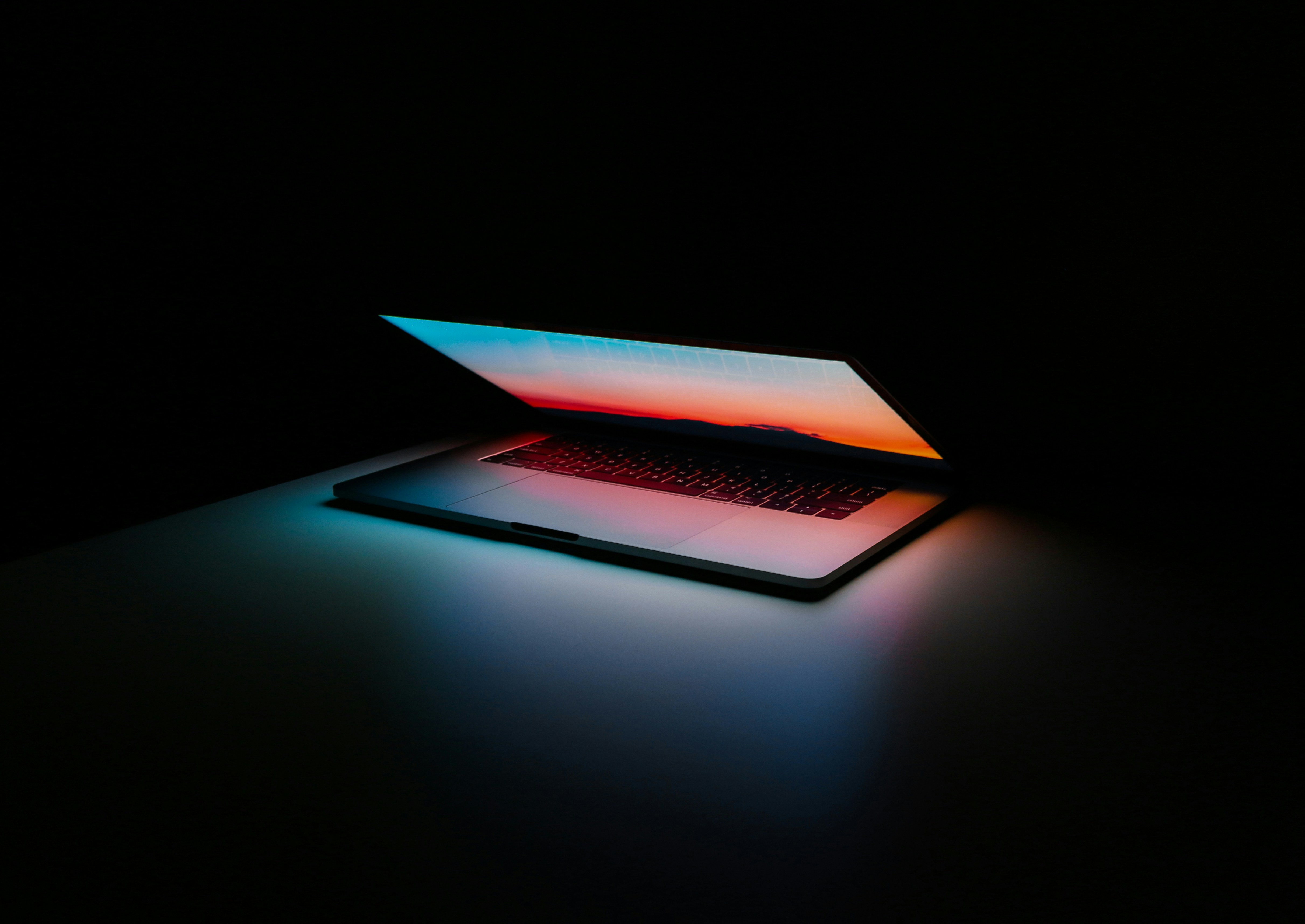 Partially open laptop on a dark surface with screen displaying a colorful sunset gradient.