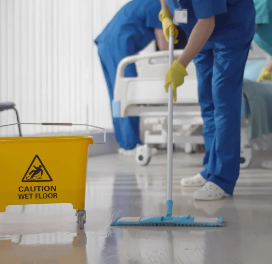 Two healthcare cleaners mopping clinical floor with wet floor sign