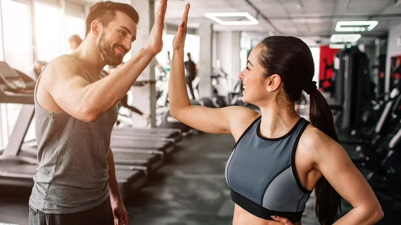 A beautiful girl and her well-built boyfriend are greeting each other with a high-five. They are happy to see each othr in the gym. Young people are ready to start their workout