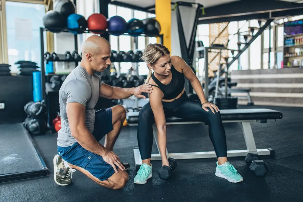 Two people, man fitness trainer and woman trainee in gym, weightlifting training.