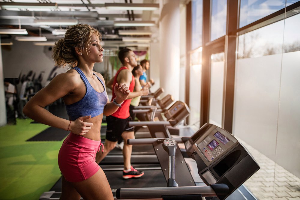 Group of athletic people running on treadmill in health club. Focus is on foreground, on young  woman.