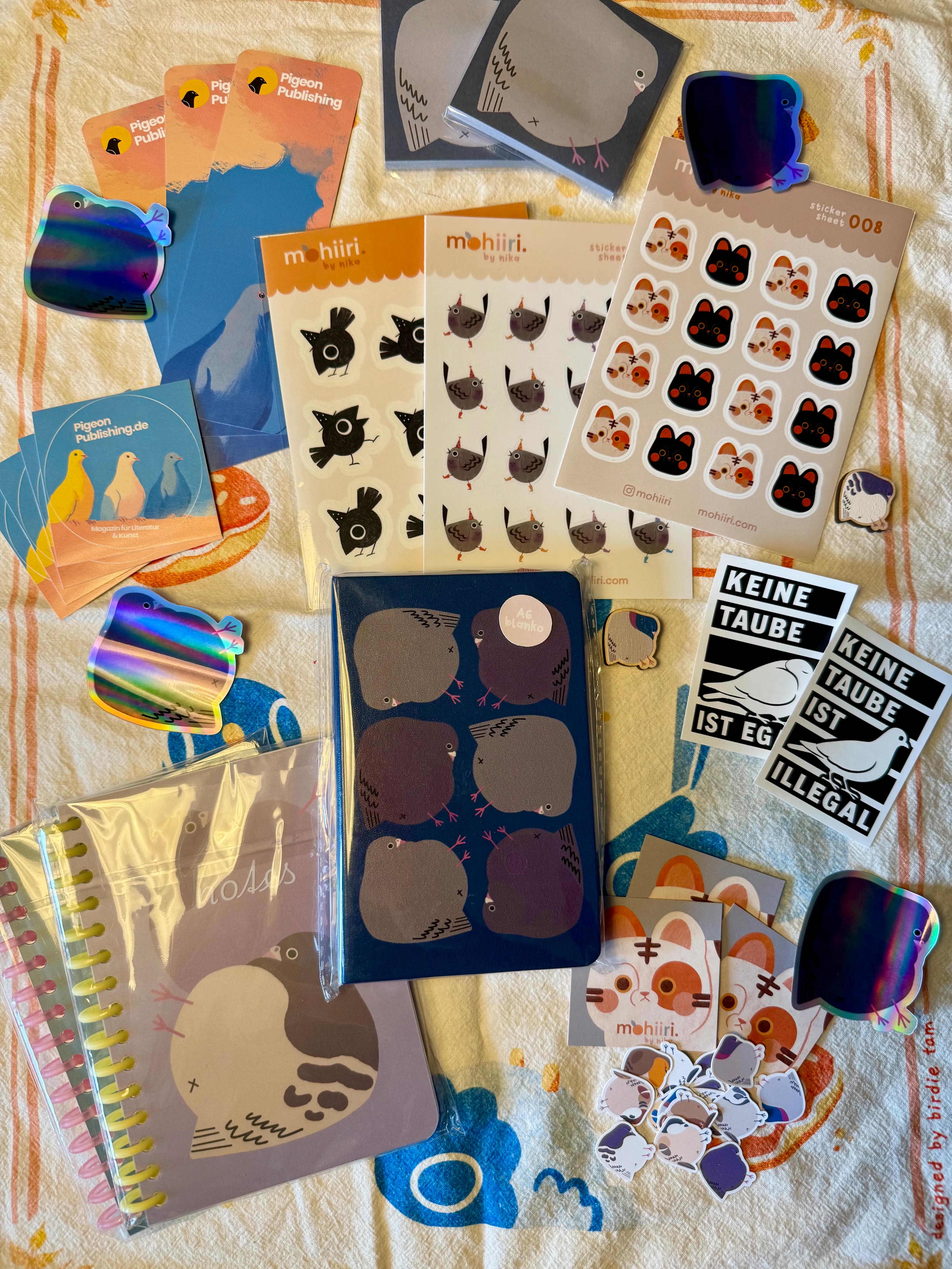 Mehrere Bücher, Sticker und Karten mit LGBTQ+- und Vogelmotiven, darunter 'You Don't Look Gay' und 'Mehr als binär'.