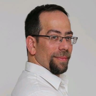 Man with glasses and a short beard wearing a white shirt, looking at the camera with a slight smile.