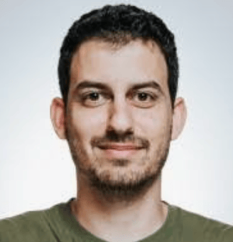 Man with short curly dark hair and a trimmed beard wearing a green shirt, smiling slightly against a plain light background.