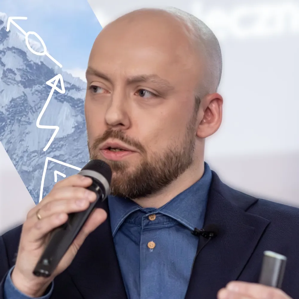 Rafał Żebrowski, trzymając mikrofon i przemawiając, symbolizuje swoje doświadczenia z zakresu autoprezentacji i budowania marki osobistej.