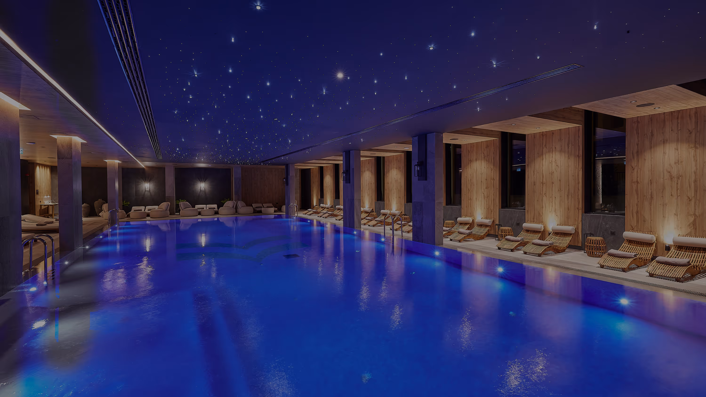 Indoor swimming pool with blue lighting, wooden walls, lounge chairs, and a starry ceiling design.