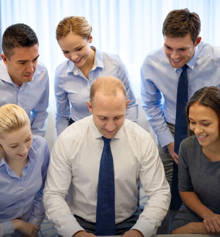 Ofis ortamında bir masanın etrafında toplanmış, gömlek ve kravat giymiş, birlikte bir şeyler inceleyen altı iş insanı.