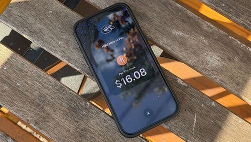 A smartphone displaying a $16.08 payment total on a wooden table