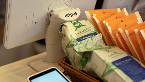 Dripos self-order kiosk beside bags of coffee beans