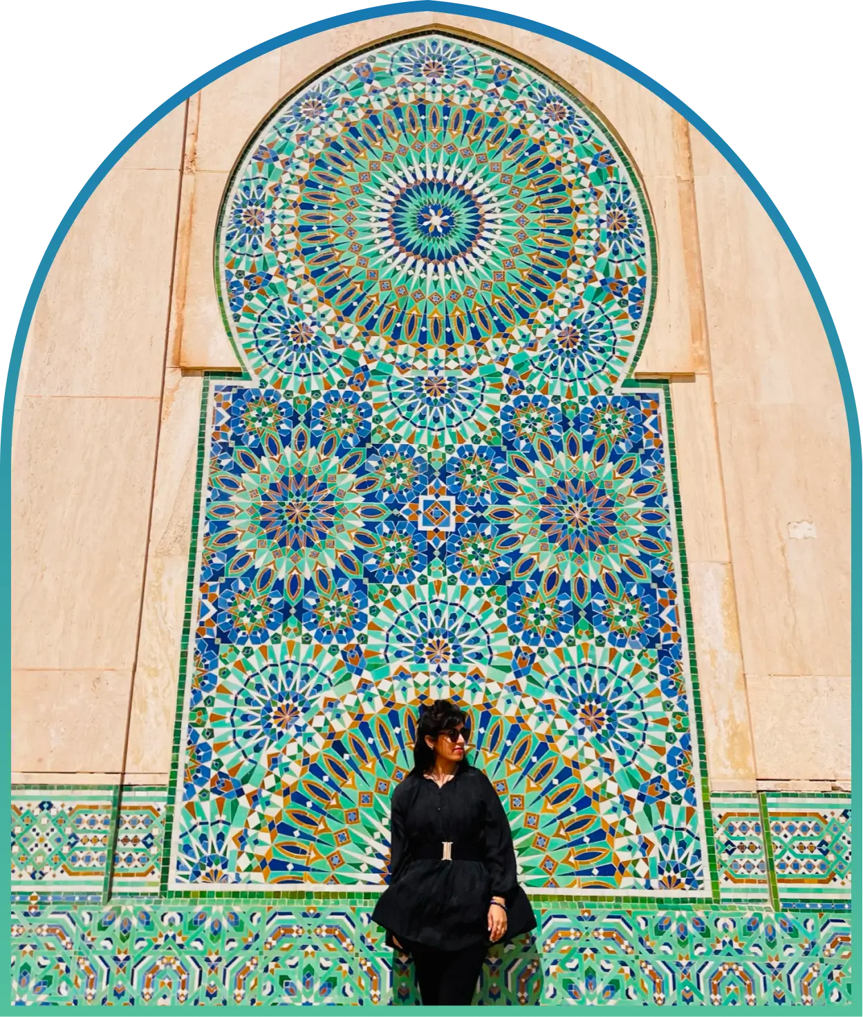 A woman in black stands in front of a large, colorful Moroccan-zellige tile mosaic with intricate geometric patterns.