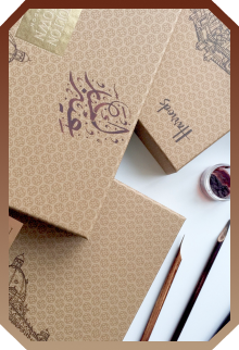 Decorative brown gift boxes with intricate patterns and calligraphy, accompanied by artist's tools and a small jar of paint.