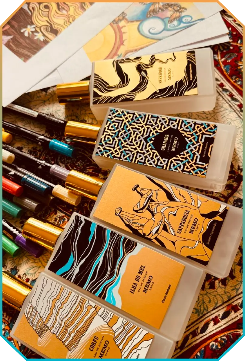 Four Memo Paris perfume bottles with colorful artistic labels arranged diagonally on a patterned surface alongside colored pens and printed artwork.