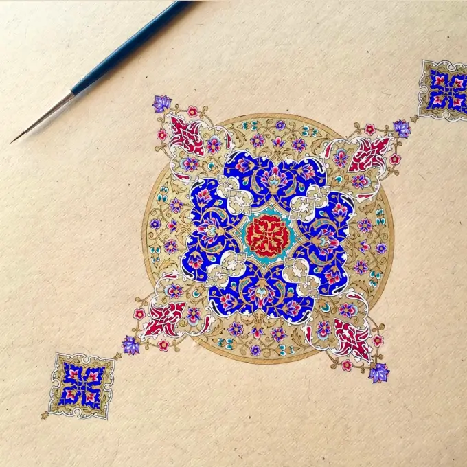 Intricate circular artwork featuring blue, red, and gold floral patterns on beige paper with a fine paintbrush nearby.