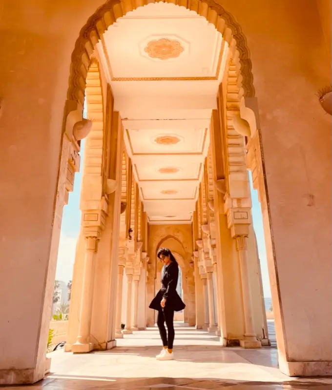 Person wearing black standing under a series of ornate stone arches in warm sunlight.
