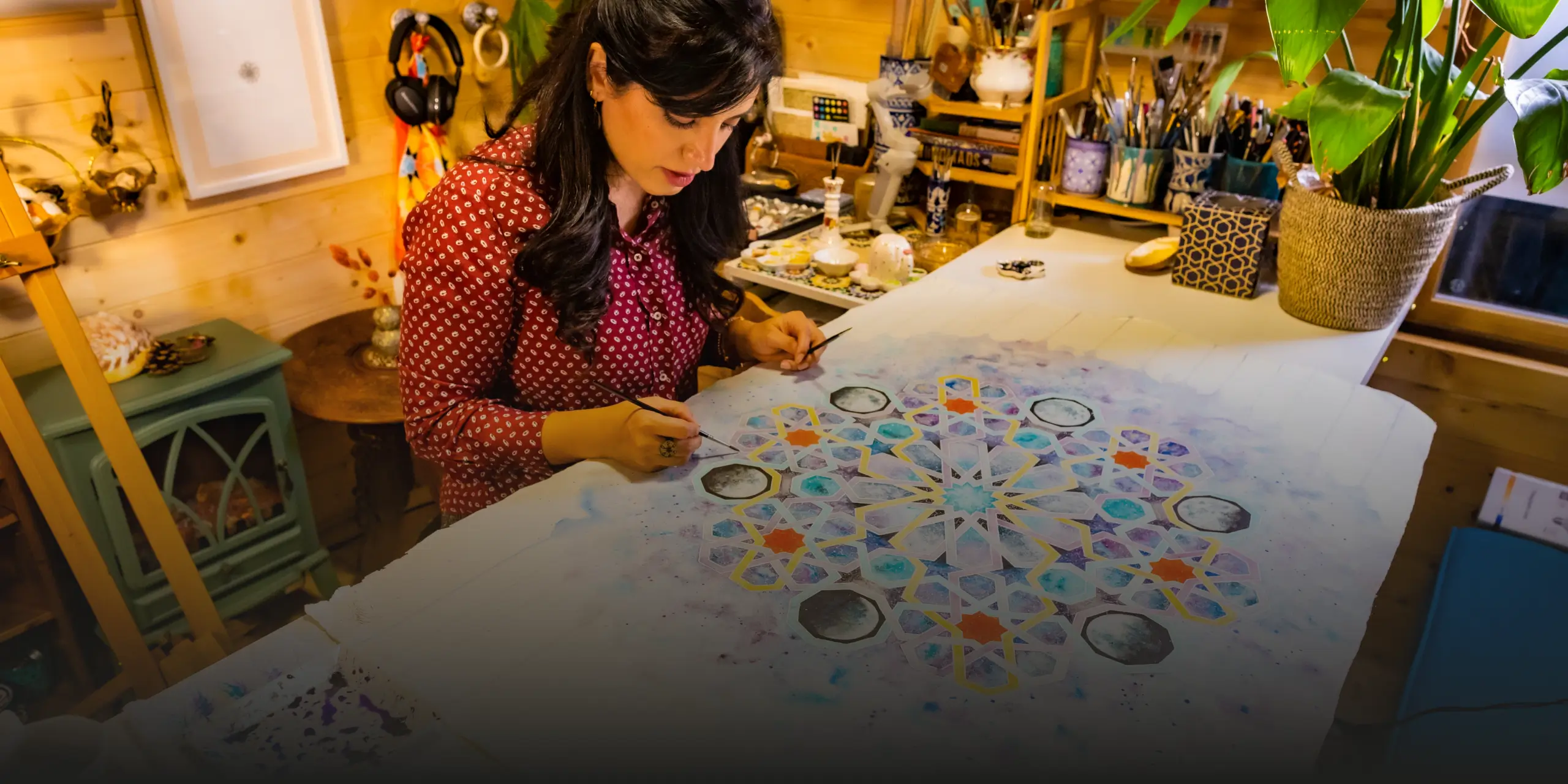 Woman painting a detailed geometric pattern on a large canvas in a cozy, well-lit art studio.