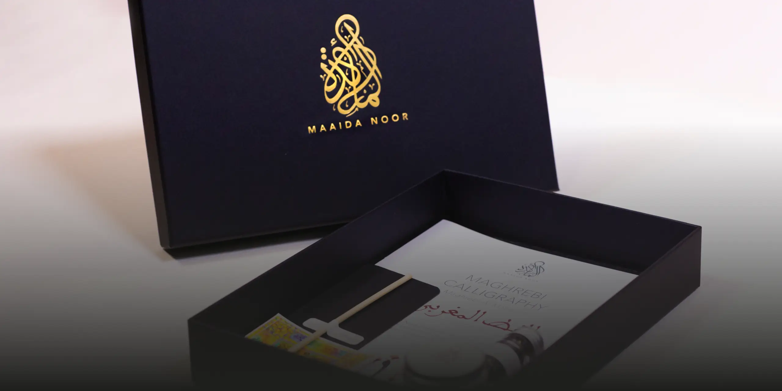Open black calligraphy kit box with a white booklet titled 'Maghrebi Calligraphy' and the brand name Maaida Noor in gold on the lid.