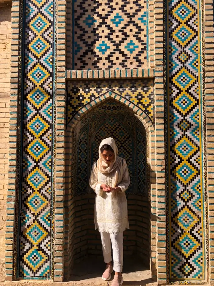 Woman dressed in white standing in an archway with colorful mosaic tile patterns in blue, yellow, and black.