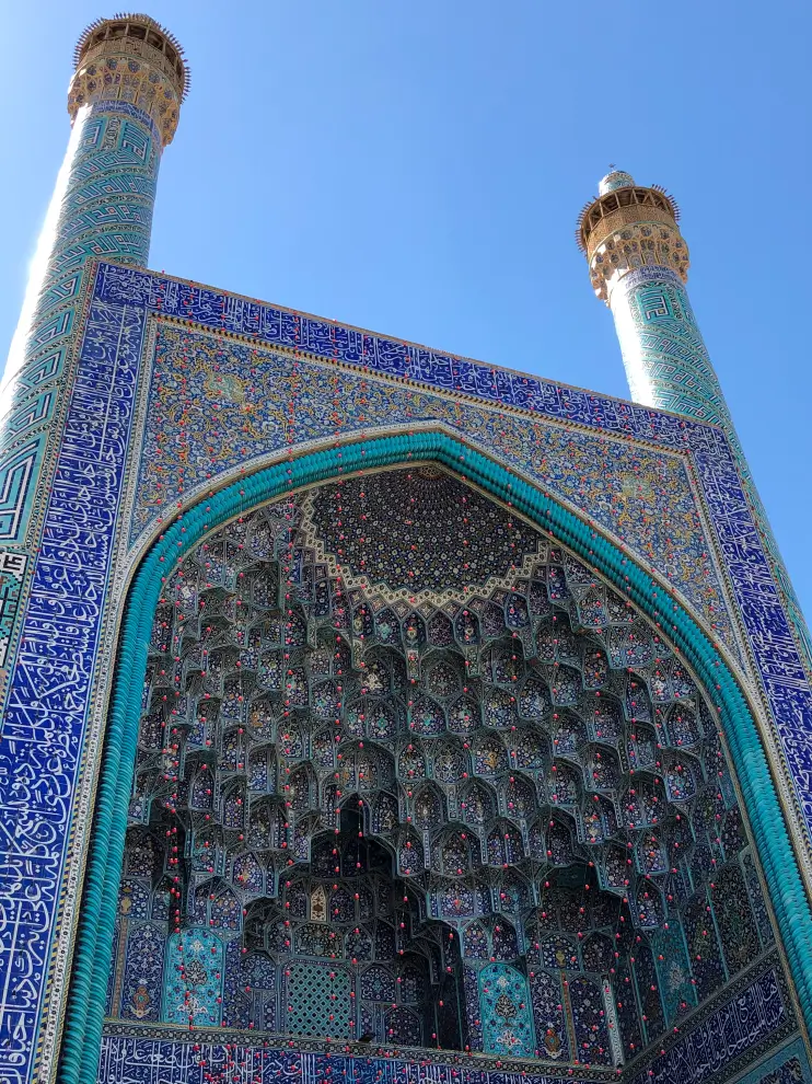 Intricately tiled entrance of a mosque with two minarets against a clear blue sky.