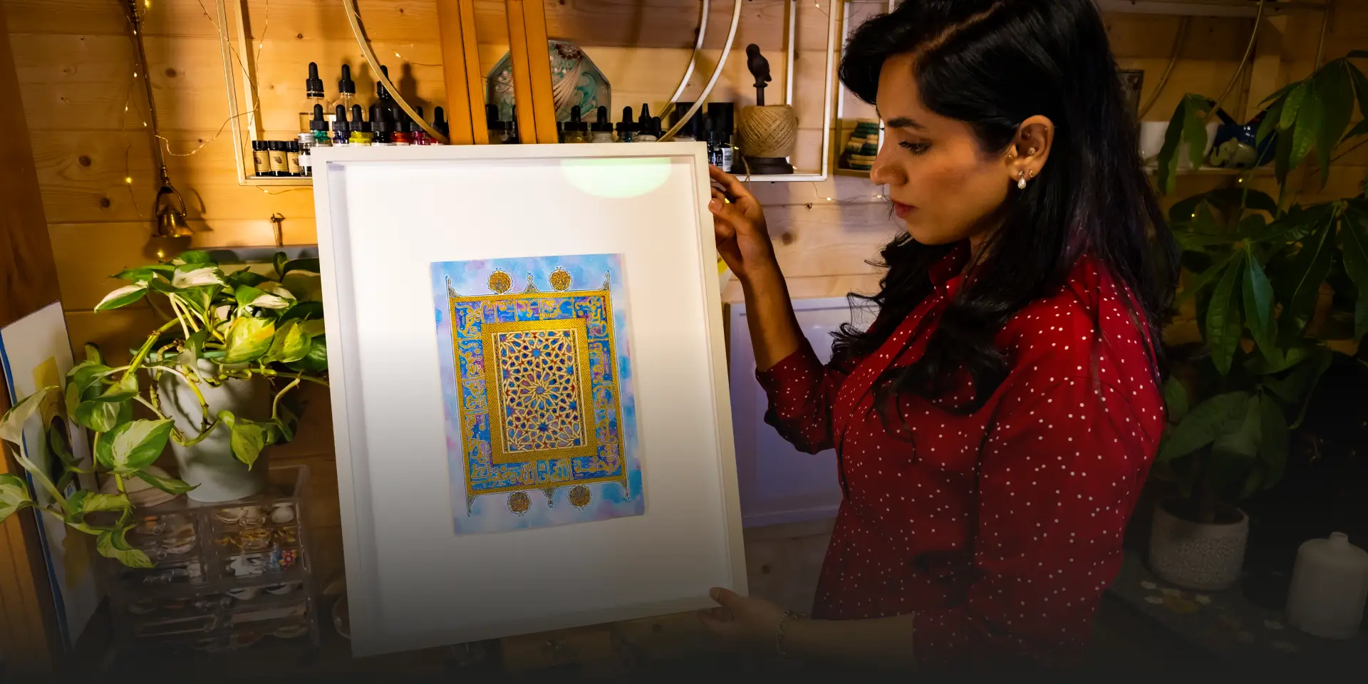 Woman in a red polka dot shirt holding a framed artwork with intricate gold and blue geometric patterns.