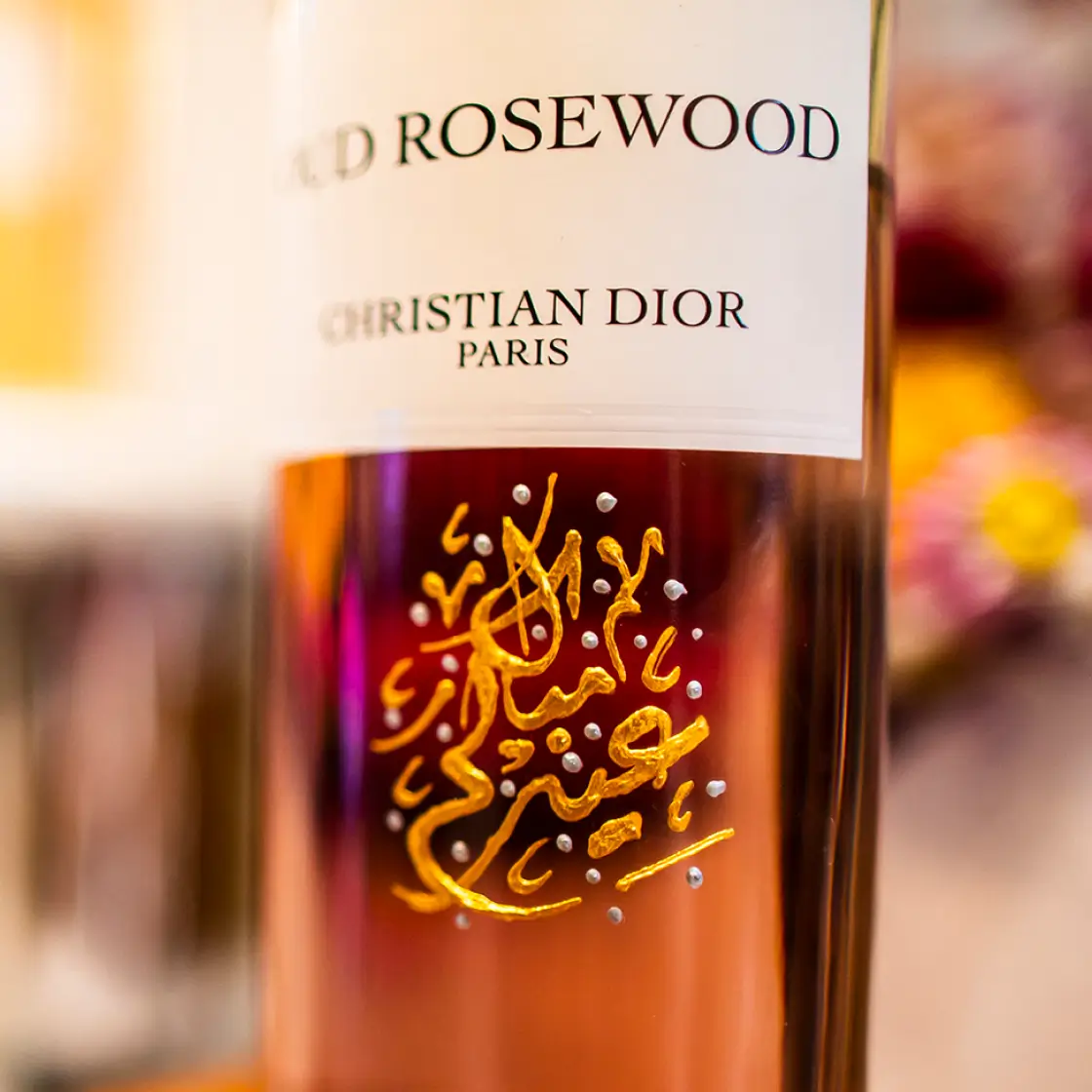 Close-up of a Christian Dior perfume bottle labeled 'Oud Rosewood' with golden Arabic calligraphy on the amber-colored glass.