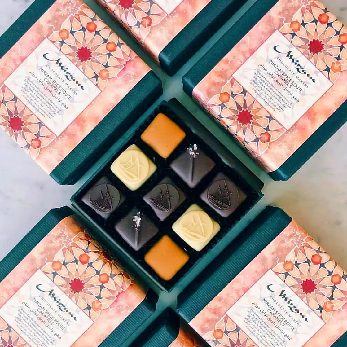 Box of assorted Mirzam Chocolates with geometric patterned packaging and nine chocolates in caramel, white, and dark varieties.