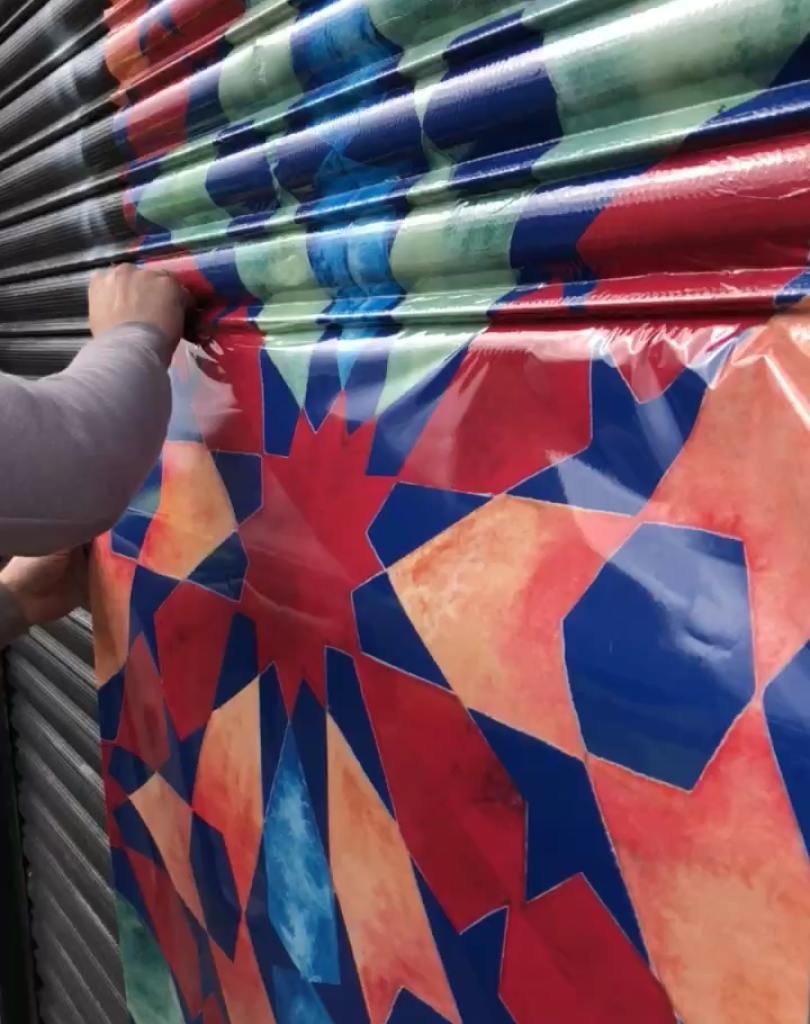 Detailed view of a hand smoothing down a patterned vinyl wrap onto the ridges of a metal security shutter.
