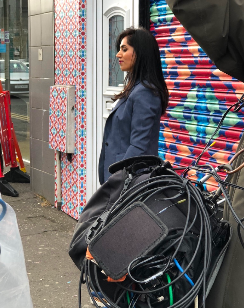 A woman standing in front of a building exterior that has been fully covered in a colorful, repeating geometric pattern wrap.