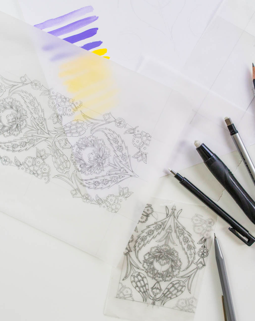 A detailed pencil sketch of a complex geometric and floral border next to purple and yellow color test swatches and drawing pens.