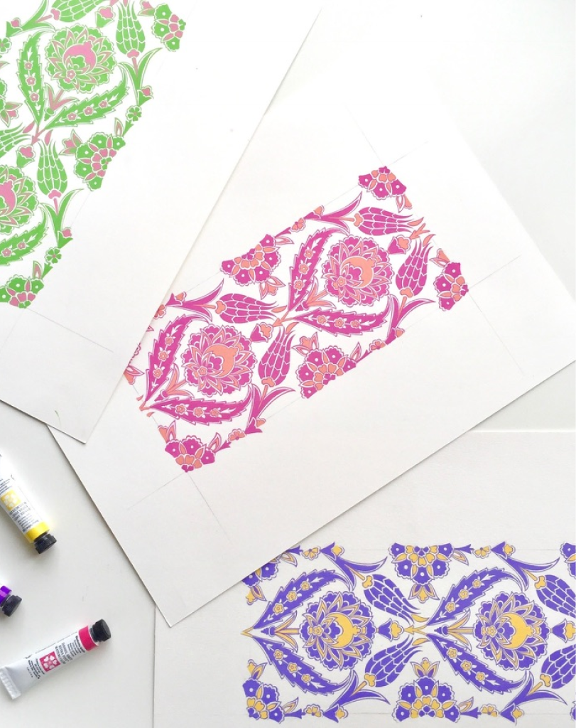Three sheets of paper showcasing completed traditional patterns in green, pink, and purple, featuring symmetrical floral and leaf motifs.