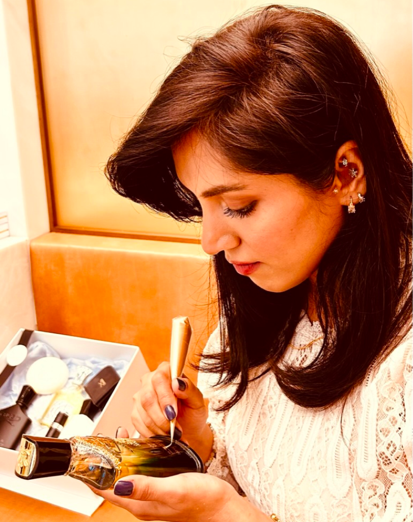 Close-up of Maadia Noor applying custom gold calligraphy to a Creed perfume bottle.